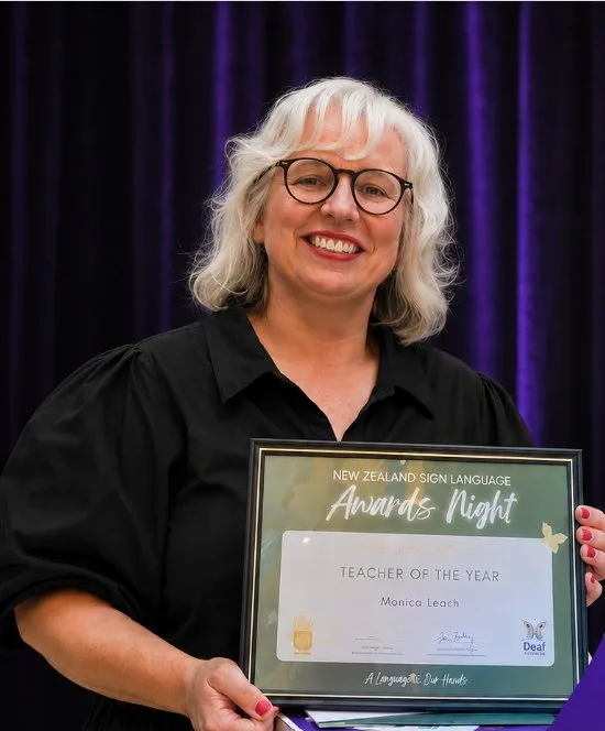 Monica Leach smiling with her New Zealand Sign Language Teacher of the Year award